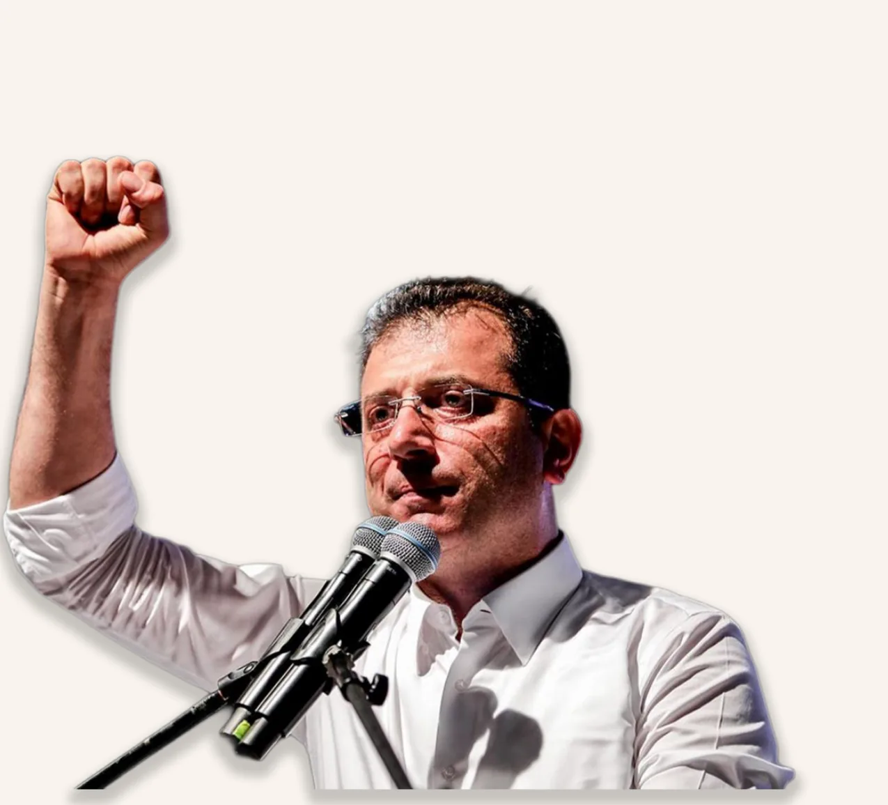 Ekrem İmamoğlu raises his fist at a microphone while addressing supporters.